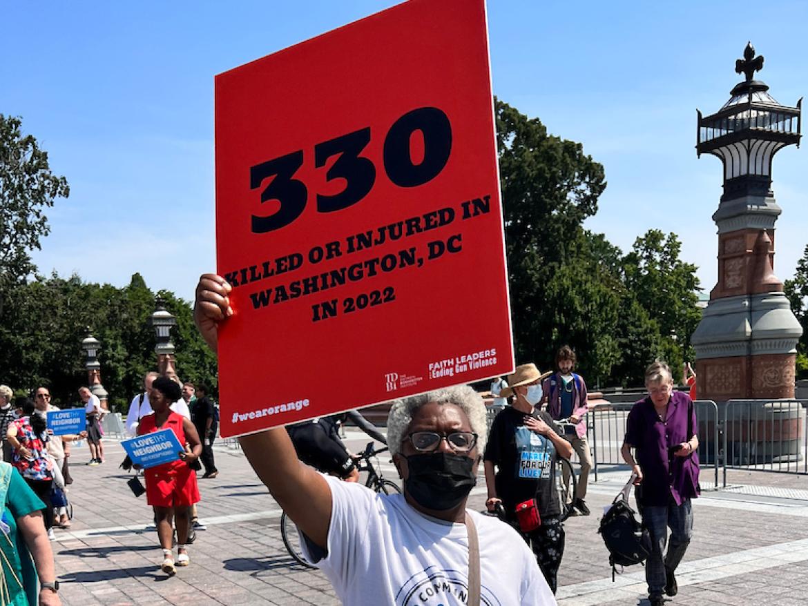 Woman holds sign that says "330 killed or injured in washington DC in 2022" in June 2022 protest