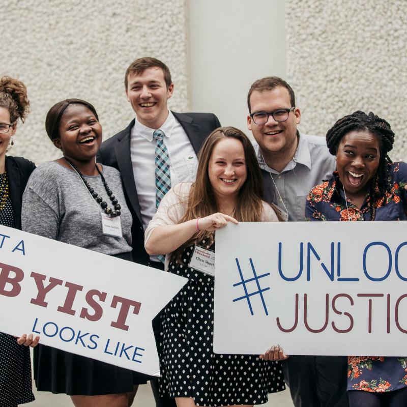 Young people hold signs that say This Is What a Lobbyist Looks Like and Unlock Justice.