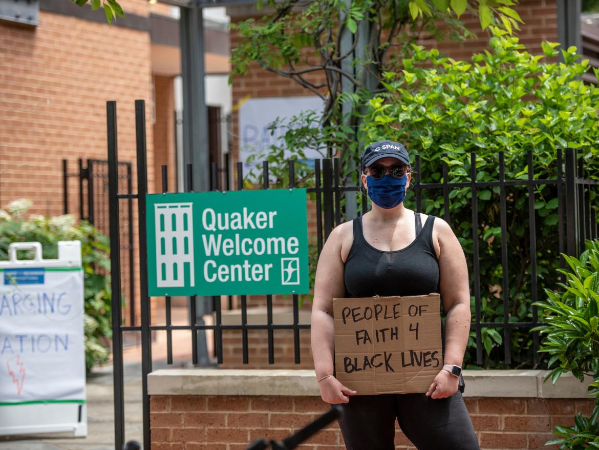 Adrienne outside Quaker welcome center holding sign that says "people of faith 4 Black lives"