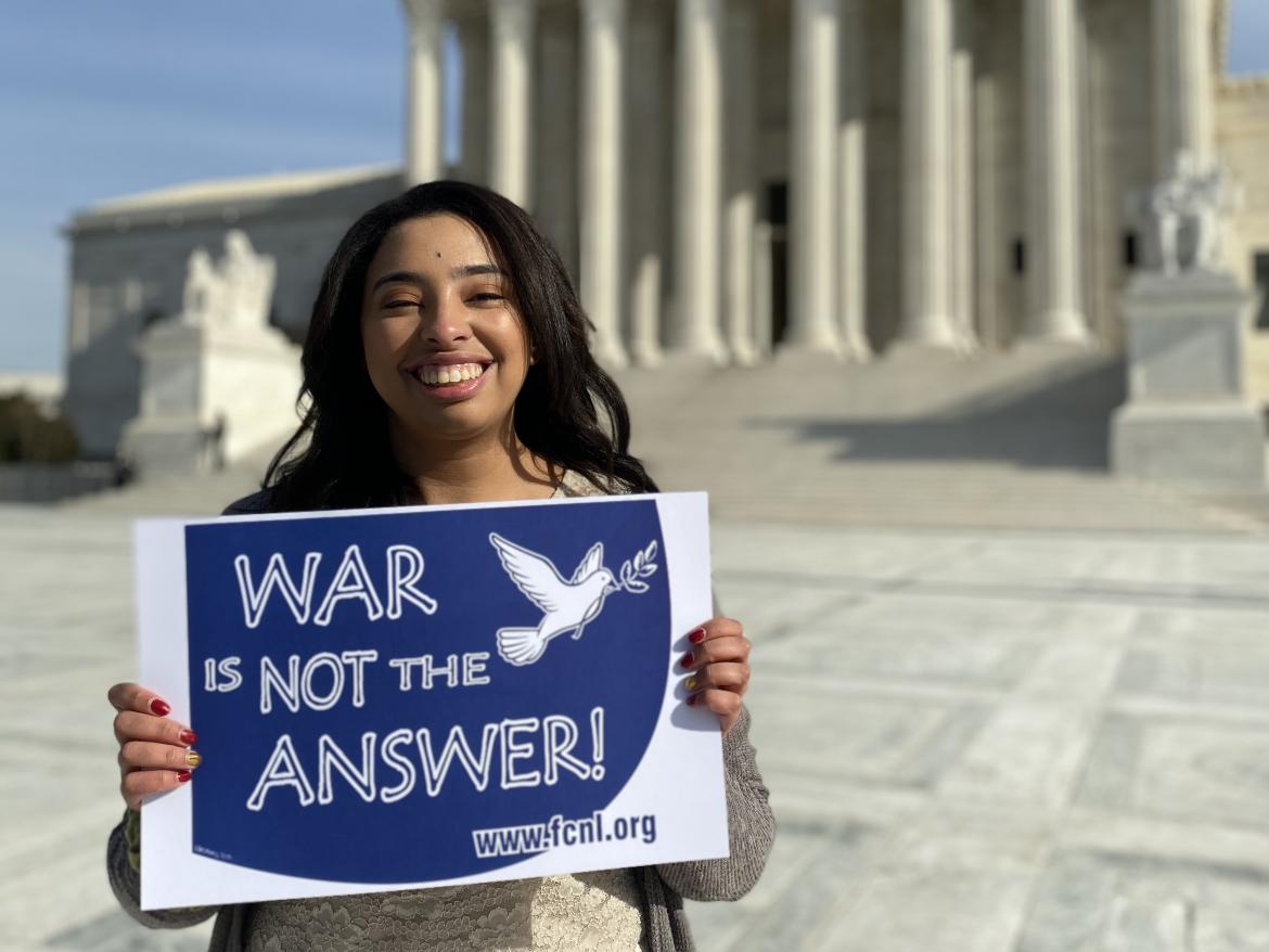 Alicia Cannon smiling holds War is Not the Answer sign in front of Supreme Court