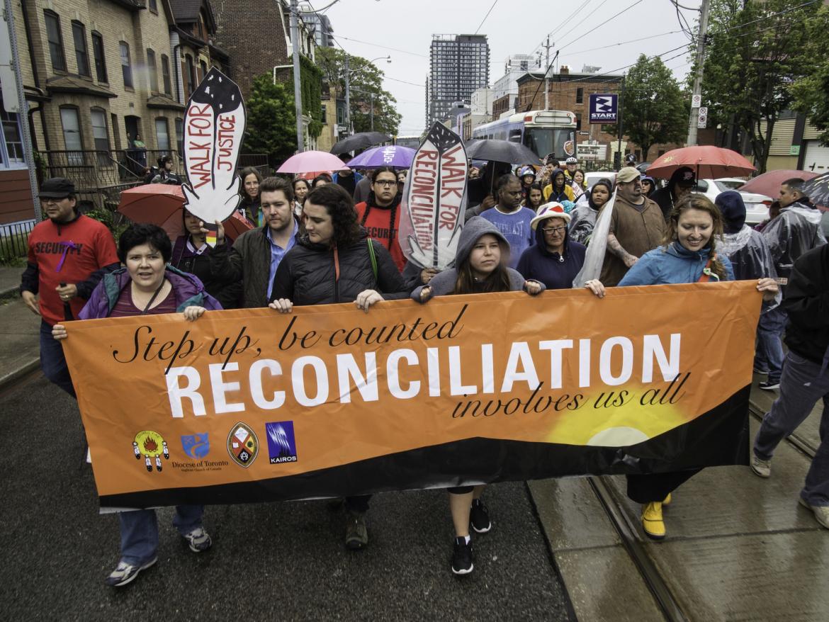 Marchers hold sign that says "reconciliation takes all of us"
