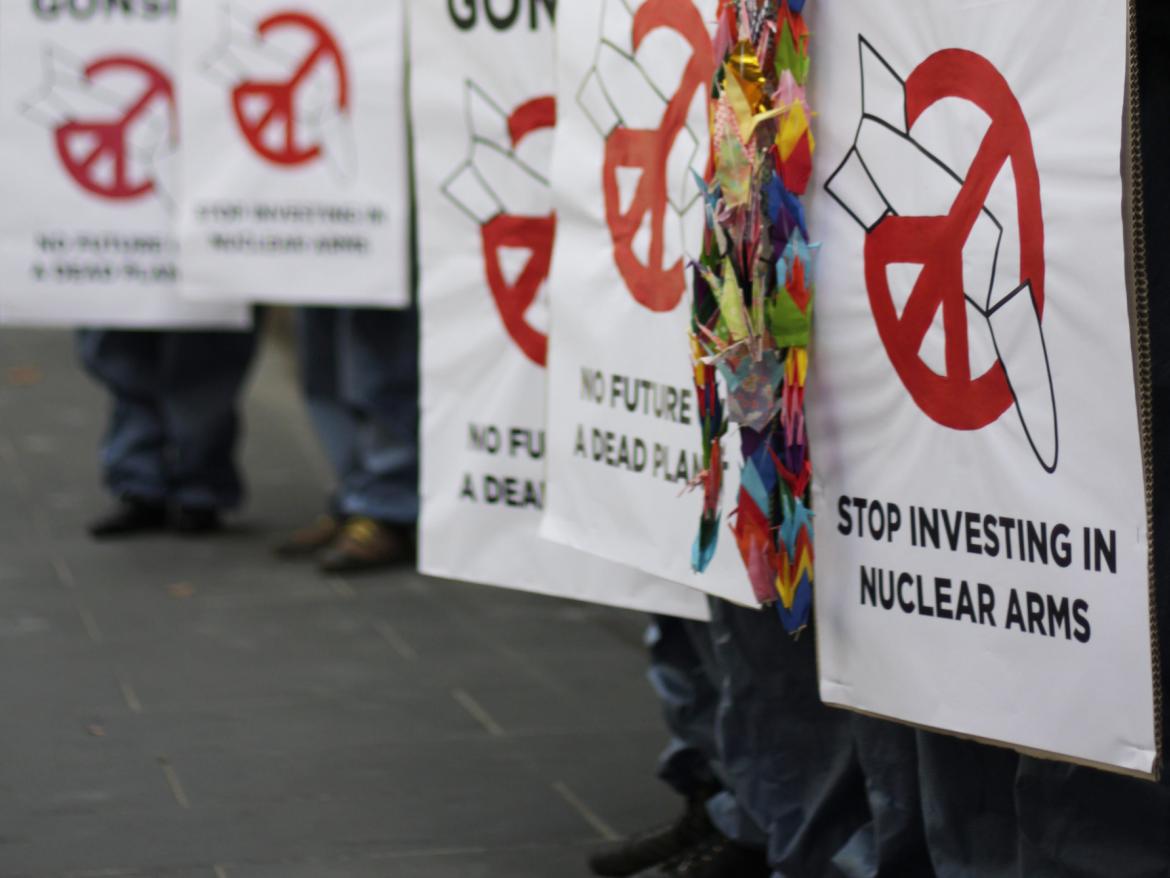 Protest signs that read "stop investing in nuclear arms"