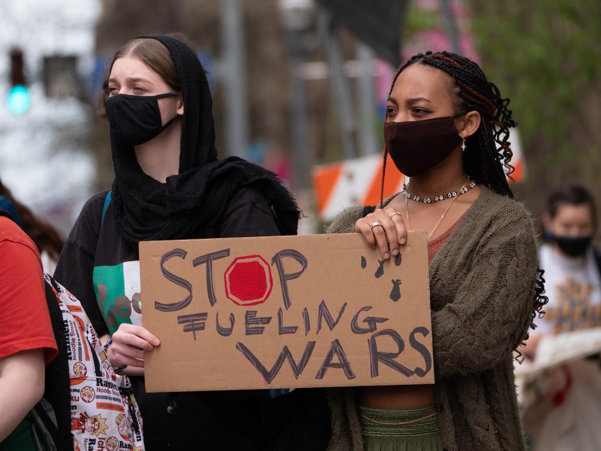 Two young women hold protest sign that reads: "Stop Fueling Wars"