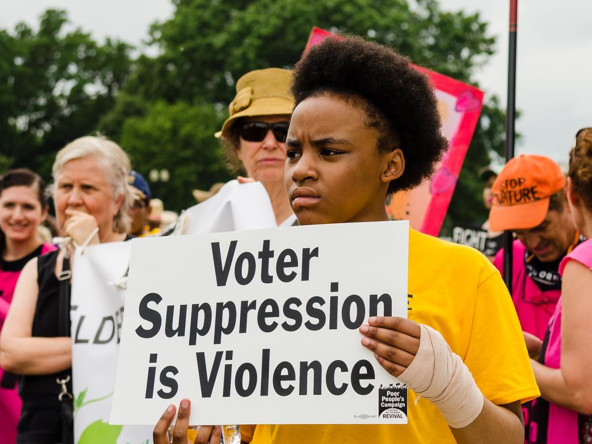 Girl at Poor People's Campaign protest holds sign that says "Voter Suppression in Violence"