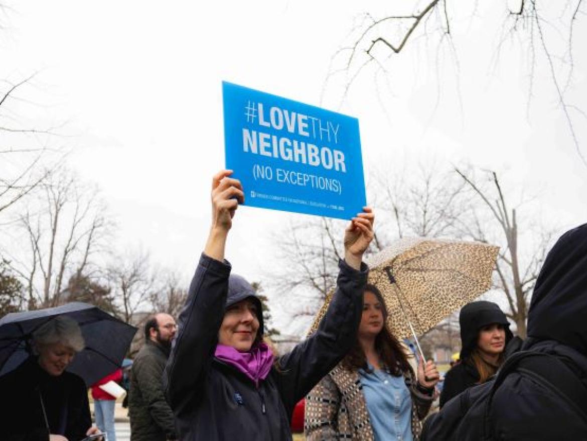 Woman holding Love Thy Neighbor sign with umbrellas in the background