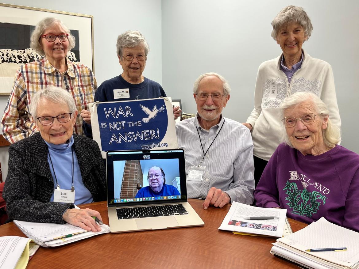 An Advocacy Team gathers around a laptop and sign saying "War is not the Answer"