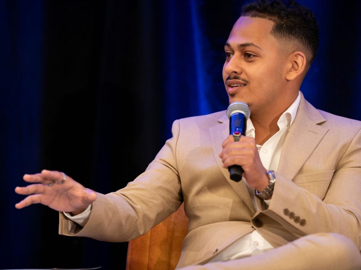 Man speaking in a tan suit into a microphone