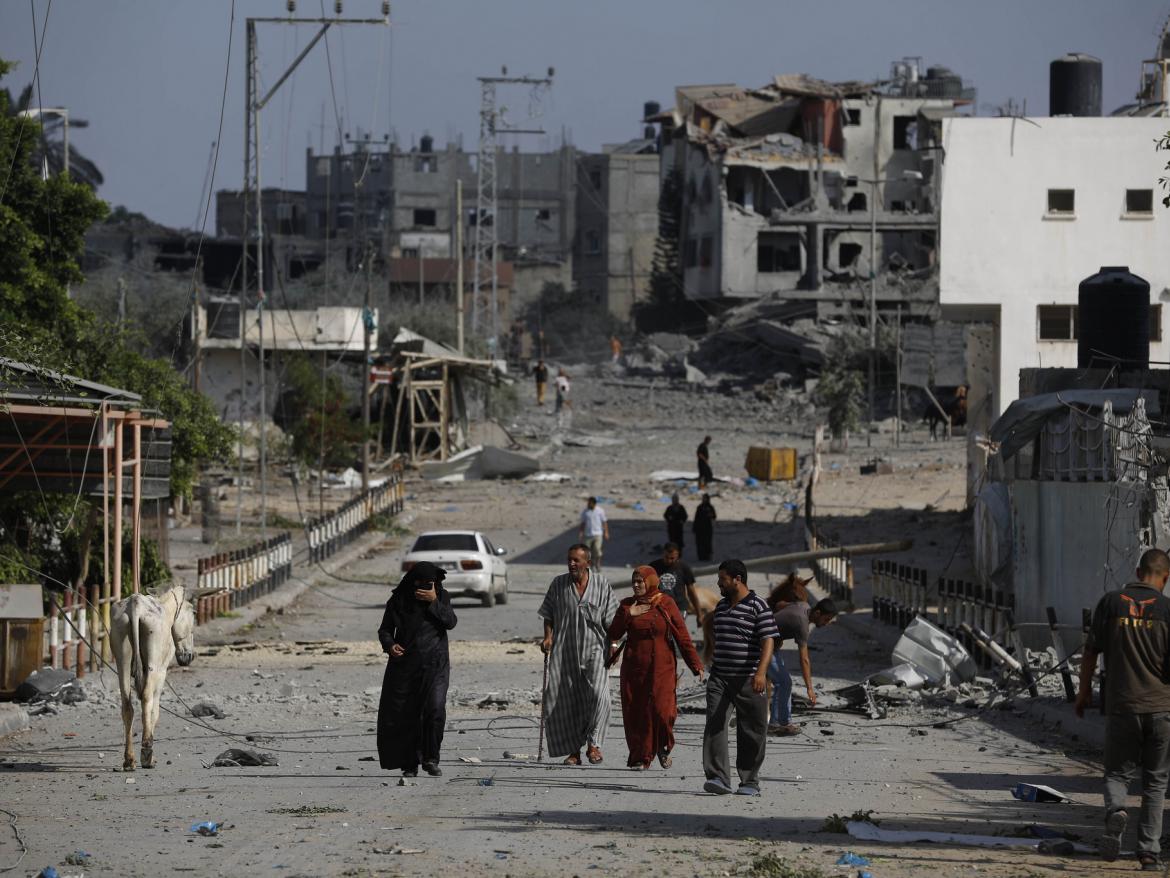 People walk in front of bombed buildings