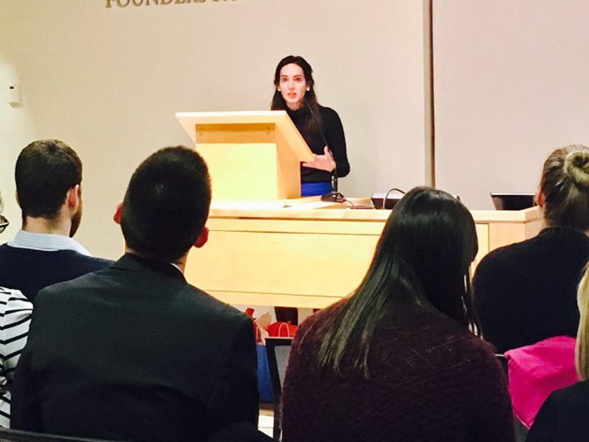 Yasmine Taeb speaks from behind a podium with audience members in the foreground.