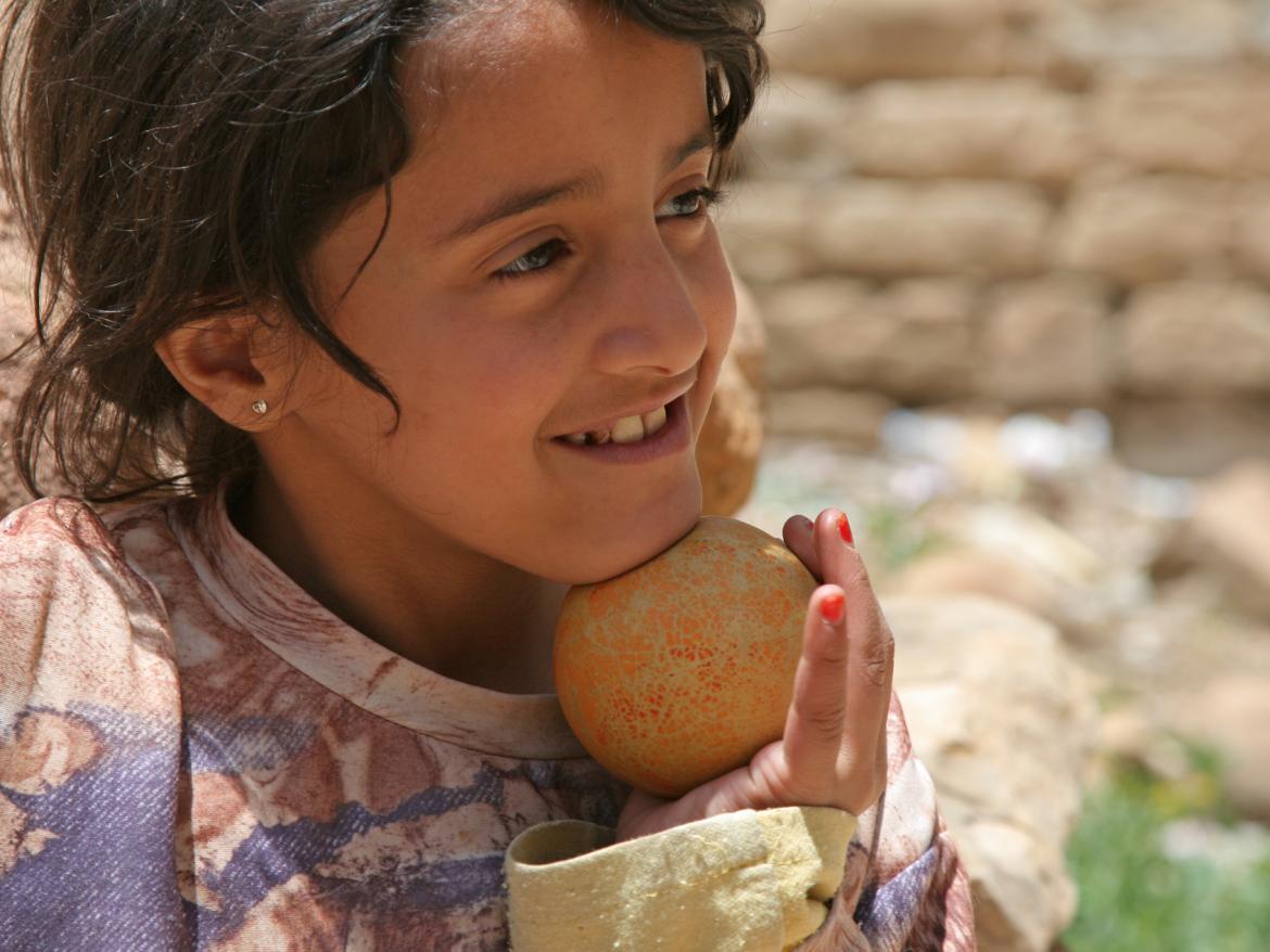 A child smiles while holding a ball and looking into the distance.