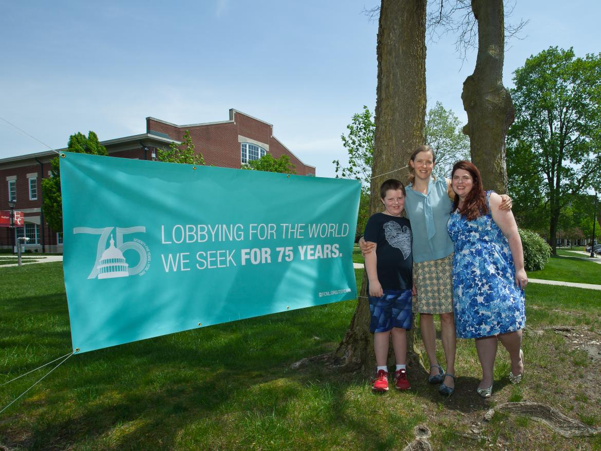 Two women and a boy stand next to a 75th anniversary sign. 