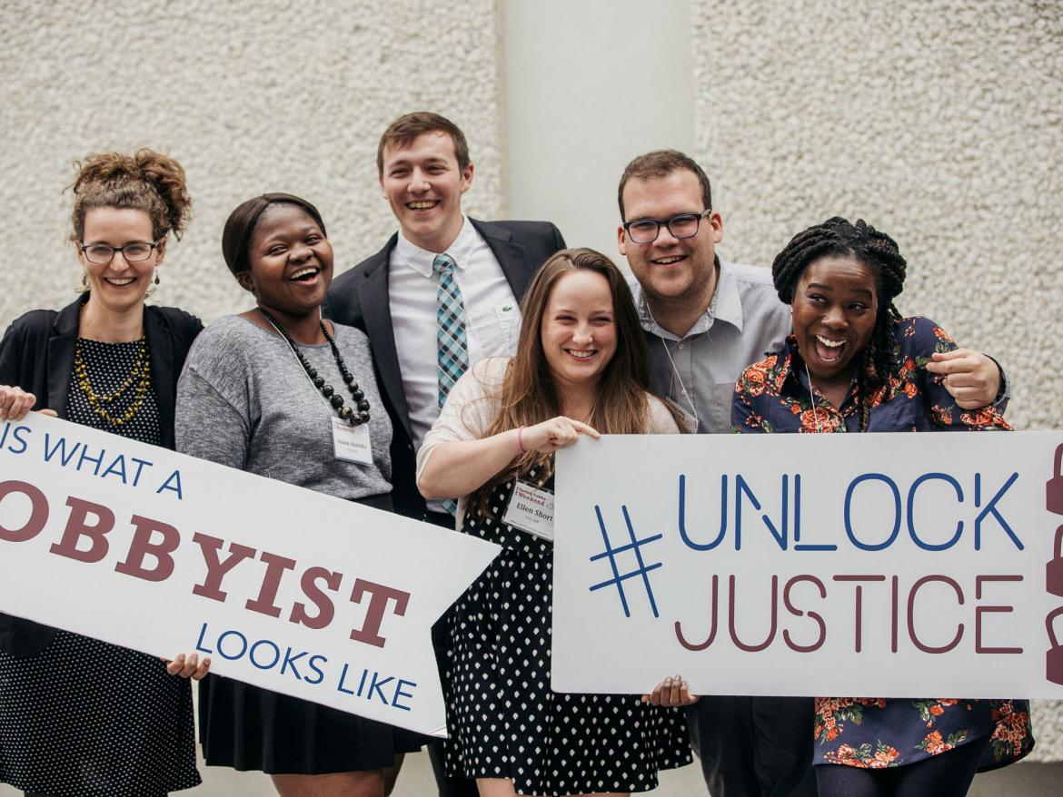 Young people hold signs that say This Is What a Lobbyist Looks Like and Unlock Justice.