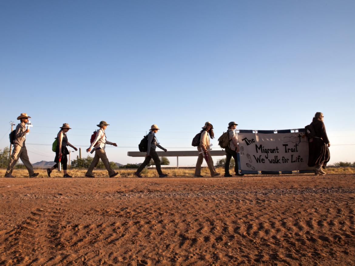 Group walks through desert with banner.