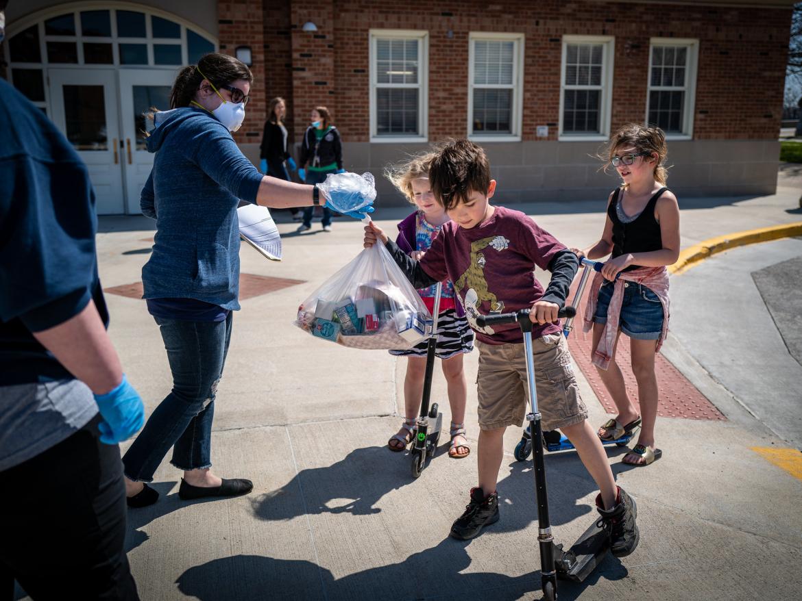 Des Moines Public Schools launched a huge increase in the number of free meal sites for students during the COVID-19 closure, going from 22 to 50 locations around the city. Here students on scooters receive a bag of food from volunteers.