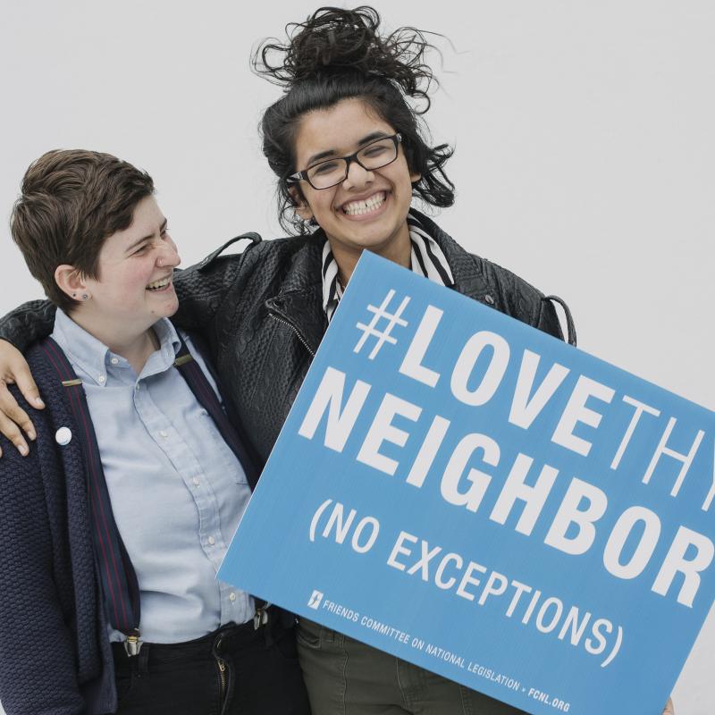 Two advocates laugh and hold a sign that says "Love Thy Neighbor"