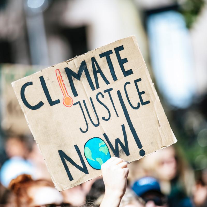 Protestor holds "Climate Justice Now" sign