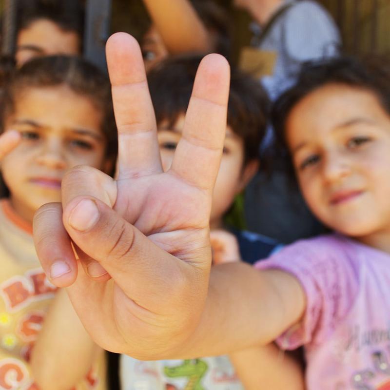 Syrian refugee children holding up peace signs in Lebanon.