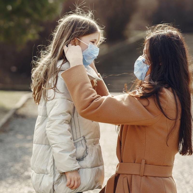 mom helps child put on facemask in park