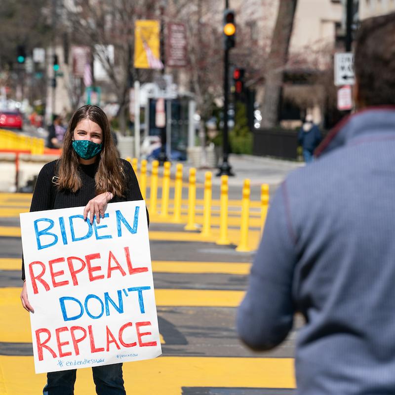FCNL advocacy teams member holding a sign that says "Biden Repeal Don't Replace" sign at AUMF repeal really