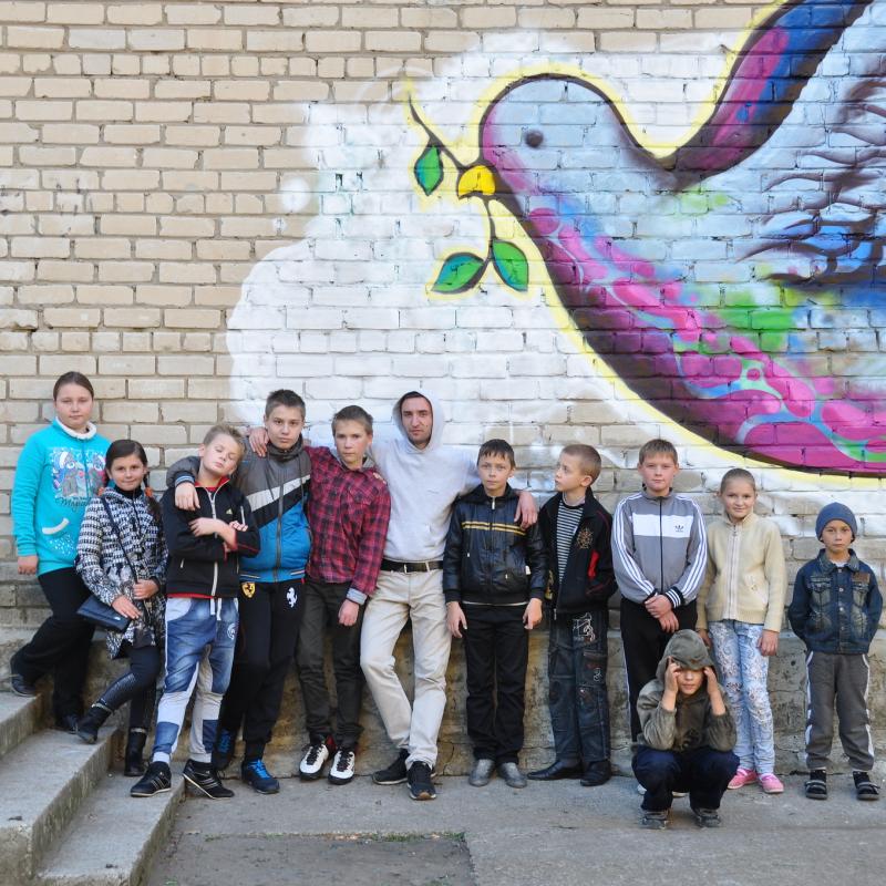 Kids in New Donbass, Ukraine stand in front of a mural depicting a peace dove