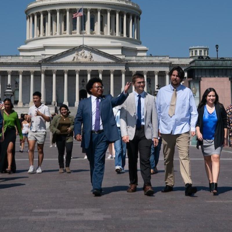 Group of young people walking toward the camera, in front of the U.S. Capitol