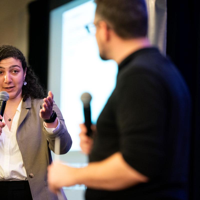 A woman speaking at a mic gesturing to a man