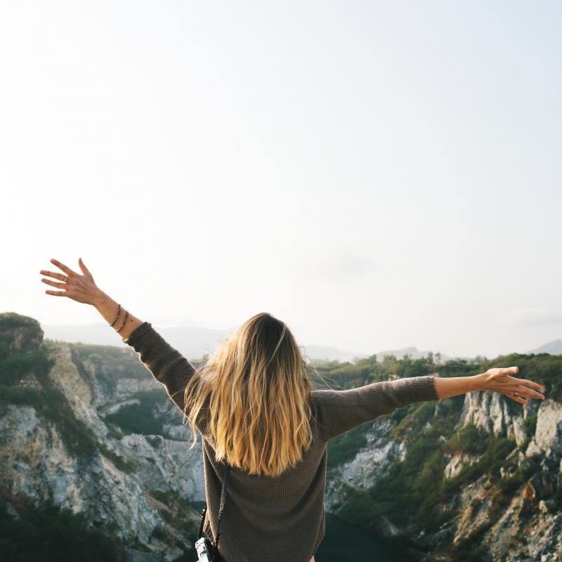 Woman standing on mountaintop with arms wide open. 