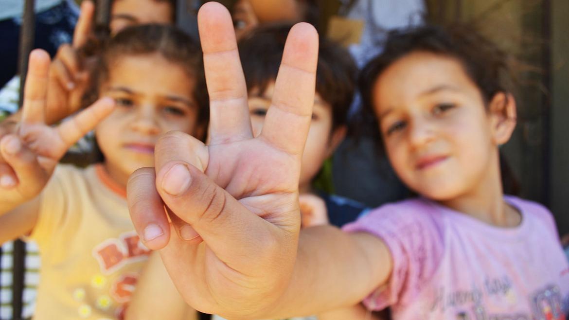 Syrian refugee children holding up peace signs in Lebanon.