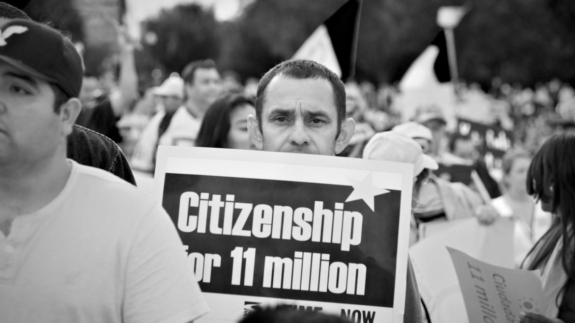 Man holding sign at rally that says "Citzenship for 11 Million"