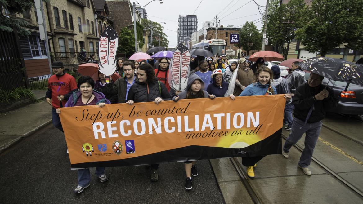 Marchers hold sign that says "reconciliation takes all of us"