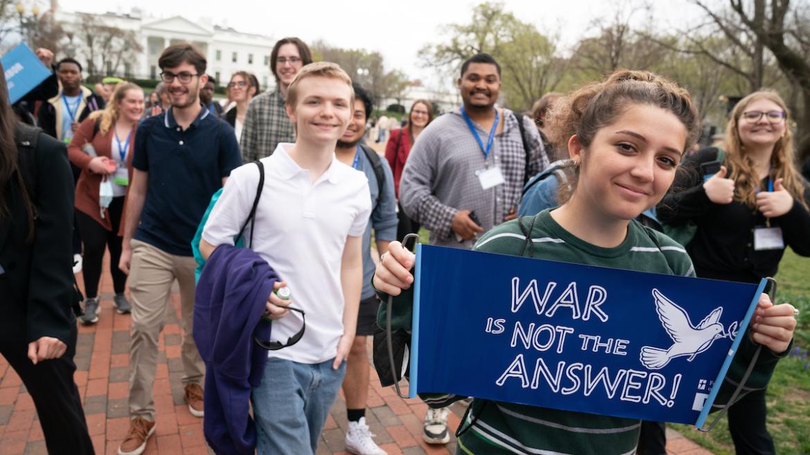Young advocates walking and smiling, hold a sign that says "war is not the answer"